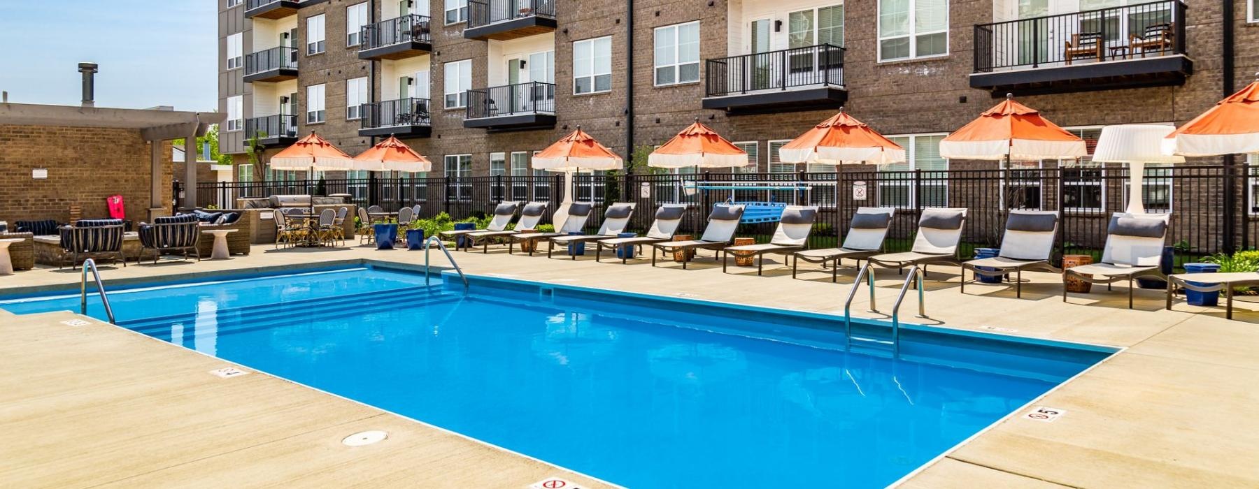 a pool with chairs and umbrellas by a building